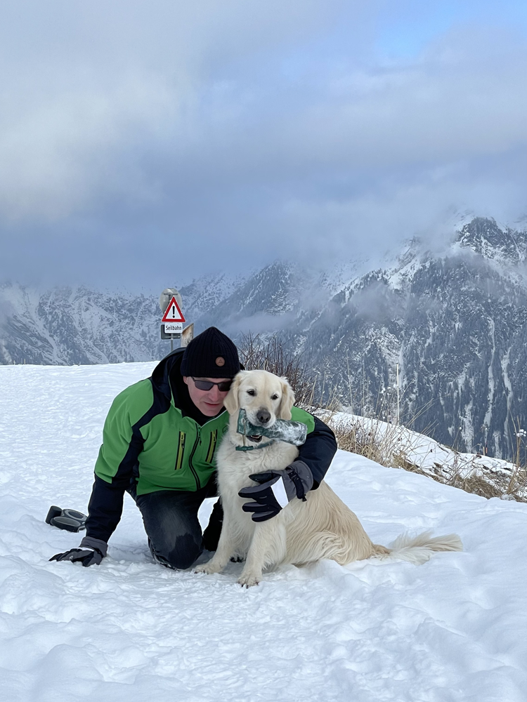 Golden Retriever Emerson in Tirol im Urlaub mit den Grumsinies Golden. Herrchen mit Emerson auf dem Wanderweg im Schnee.